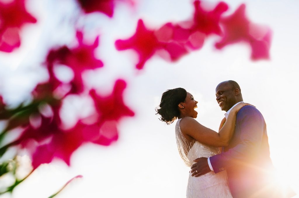 Portrait of bride and groom against a bright sky framed with pink flowes