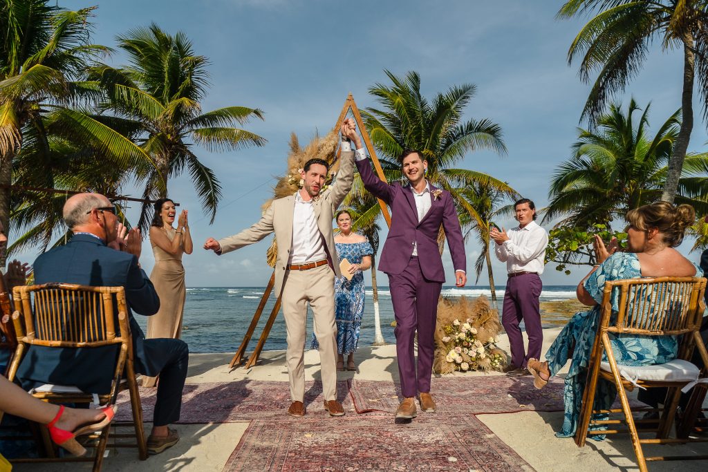 LGBTQ Wedding grooms walking out the aisle holding hands after beach ceremony in Riviera Maya photo taken by Citlalli Rico Photography